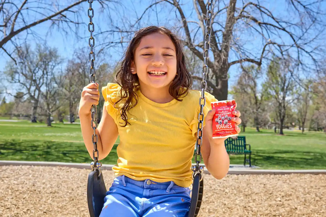 Smiling child on swing in USA park holding Nature’s Garden Probiotic Strawberry Yoggies yogurt snack pack with probiotics.