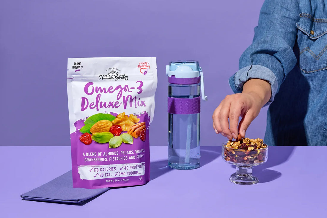 Nature’s Garden Omega-3 Deluxe Mix bag with nuts and dried fruit in USA, shown beside water bottle and hand reaching for snack.