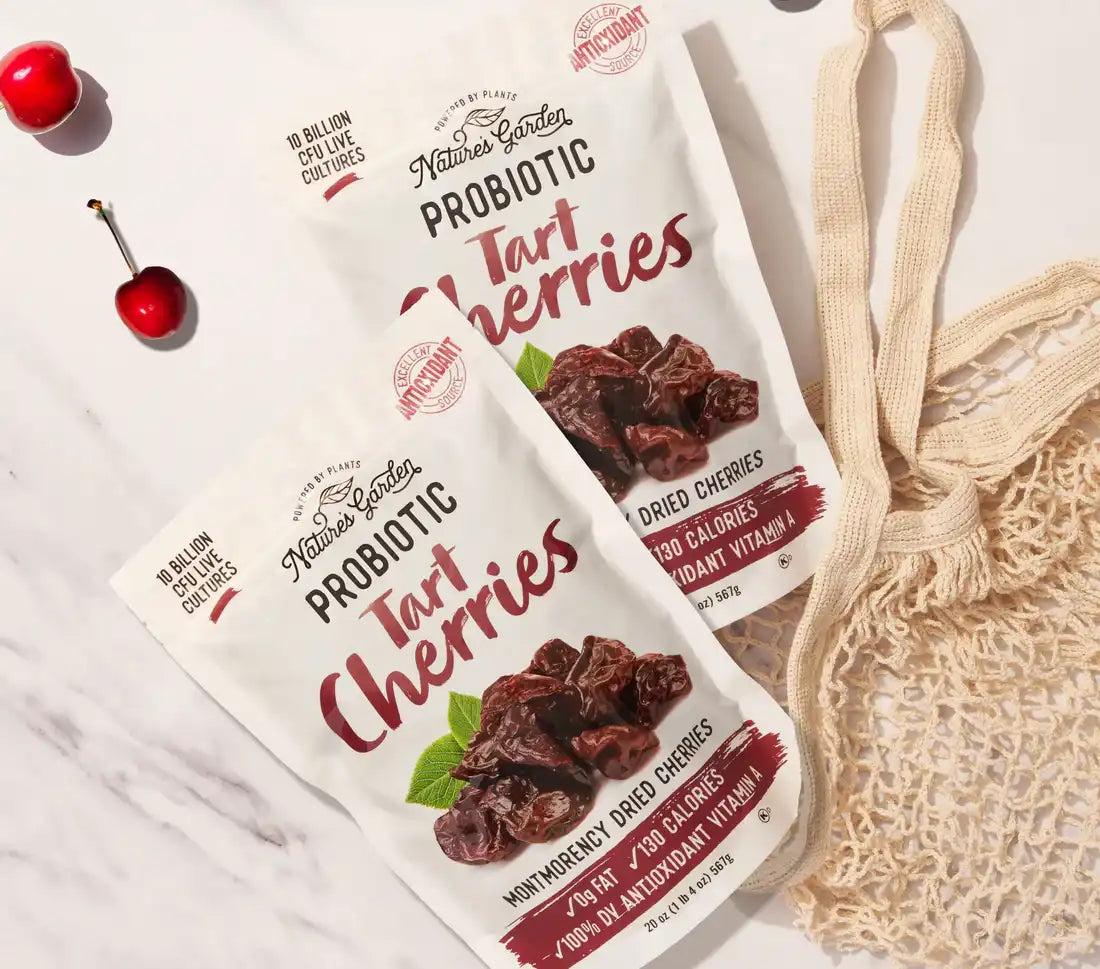 Nature’s Garden Probiotic Tart Cherries packs on marble surface with fresh cherries and a reusable net grocery bag.