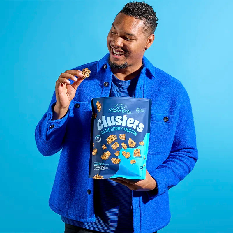 Person holding and snacking on Nature’s Garden Blueberry Muffin Clusters bag – better-for-you granola made with real blueberries