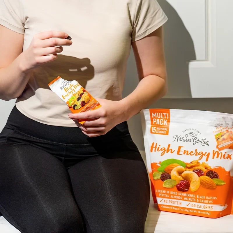Woman in workout gear enjoying Nature's Garden High Energy Mix snack pack with multipack bag beside her.