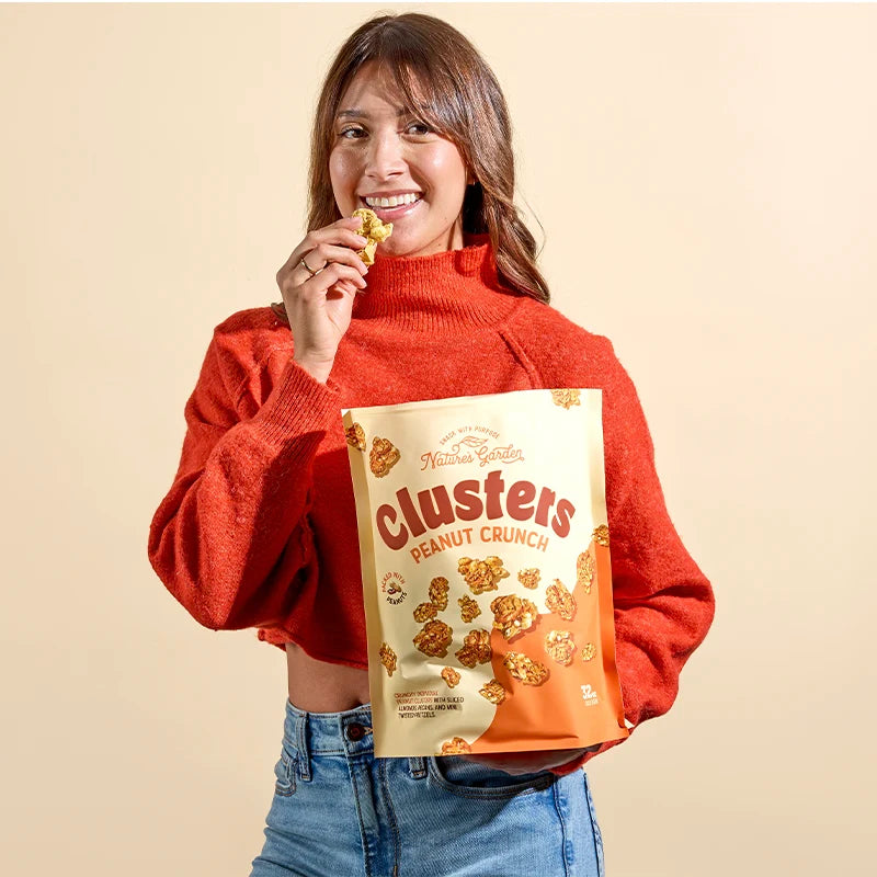 Person holding Nature’s Garden Peanut Crunch Clusters bag and eating a crunchy peanut snack – sweet and salty granola clusters
