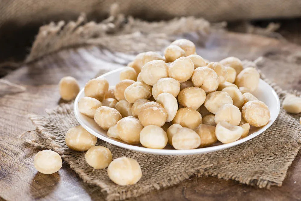 White plate filled with roasted macadamia nuts on a rustic wooden surface, ideal for crunchy and keto-friendly snacking.
