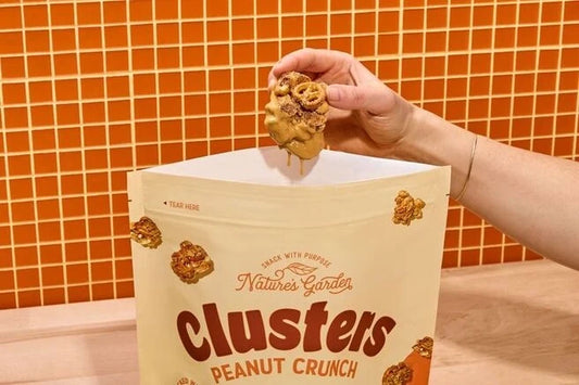 Hand holding Nature's Garden Peanut Crunch granola cluster above snack bag