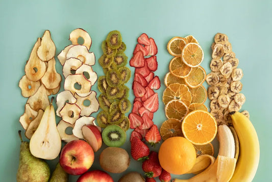 Rows of dried and fresh fruits including apples, kiwis, strawberries, oranges, and bananas arranged on a pastel background.