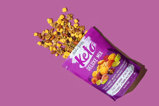 Nature’s Garden Keto Deluxe Mix spilling onto a purple surface, featuring almonds, walnuts, cheddar cheese balls, cranberries, and pistachios.