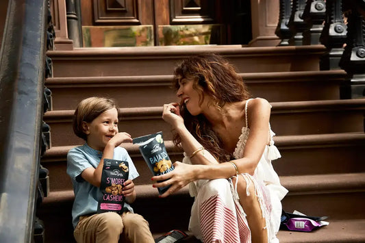 Mother and child enjoying Nature’s Garden Baja Taco and S’mores Cashews snacks while sitting on brownstone steps.