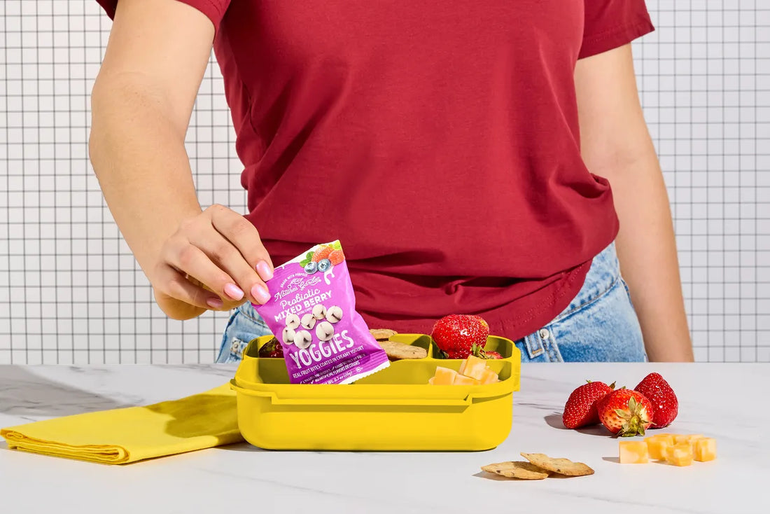 Parent packs Nature’s Garden Mixed Berry Yoggies into yellow lunchbox with strawberries, cheese, and crackers.