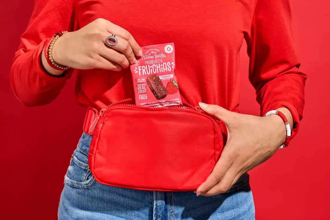 Person wearing a red shirt placing a Nature's Garden Probiotic FruChias Strawberry fruit snack into a red waist bag, showcasing a healthy on-the-go snack option.