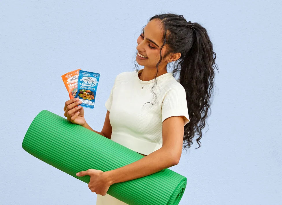 Smiling woman holding yoga mat and Nature’s Garden Probiotic snack packs in USA, promoting immune booster and omega mix.