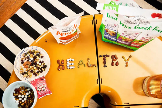 Trail mix snacks, probiotic apricots, and Yoggies arranged to spell “HEALTHY” using nuts, seeds, and dried fruit on a table.