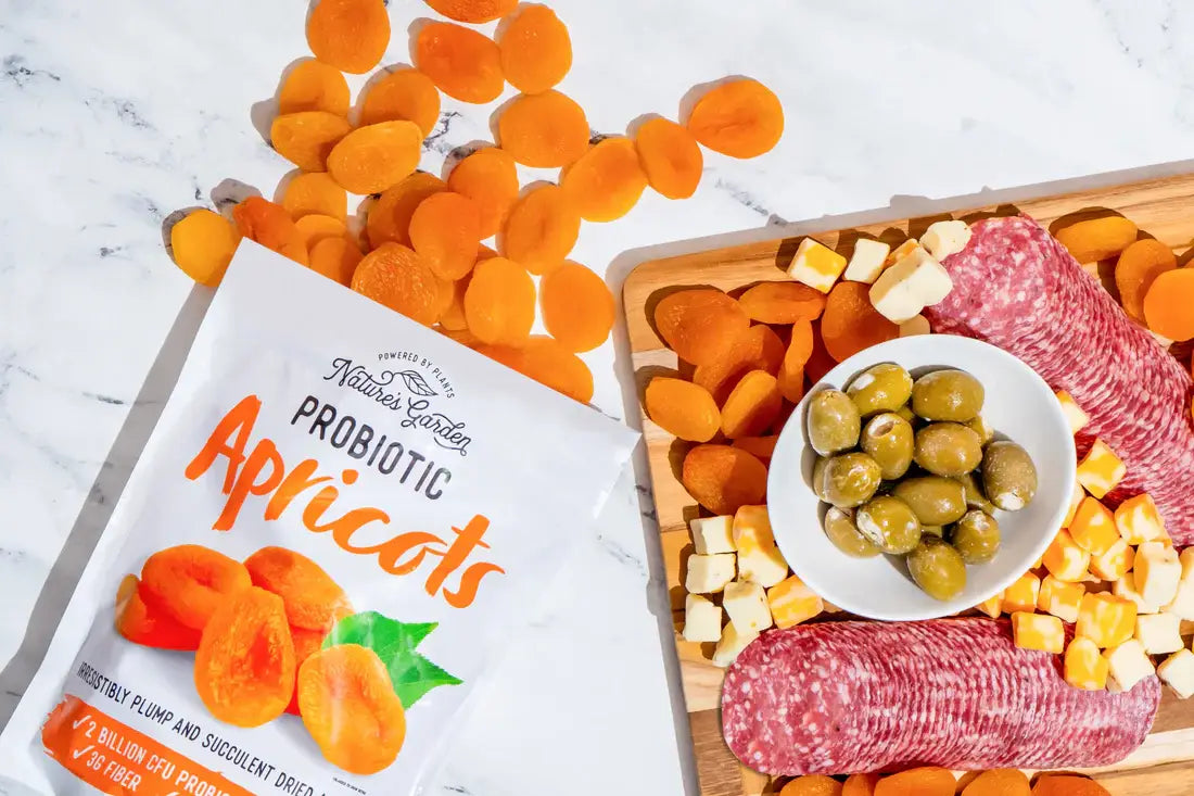Nature’s Garden Probiotic Apricots paired with a charcuterie board of cheese cubes, olives, and salami on marble surface.