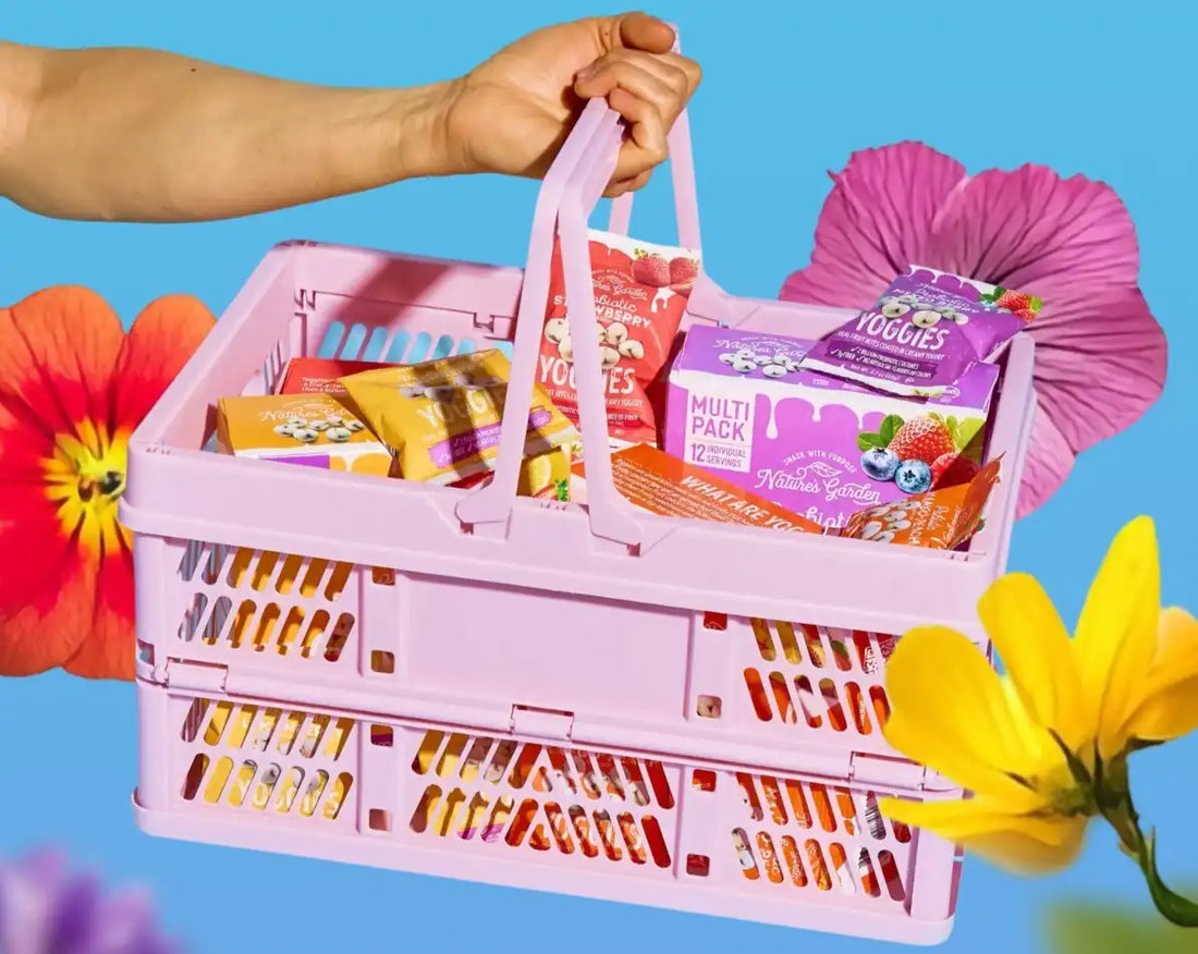 Nature’s Garden spring snack basket with Yoggies multipack and fruit snacks in a pink crate surrounded by colorful flowers.