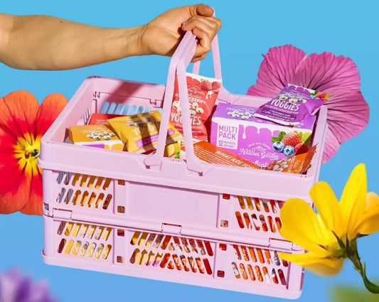 Nature’s Garden spring snack basket with Yoggies multipack and fruit snacks in a pink crate surrounded by colorful flowers.