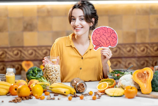 Smiling woman holding brain cutout with a table of nuts, fruits, and vegetables, highlighting foods that support energy and mental focus.