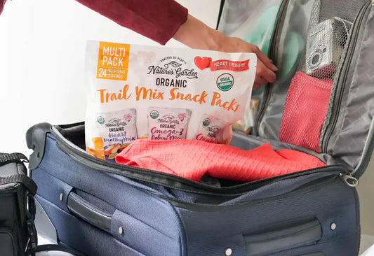 Hand packing a bag with Nature’s Garden Organic Trail Mix Snack Packs—individually wrapped, USDA Organic, heart-healthy travel snacks.