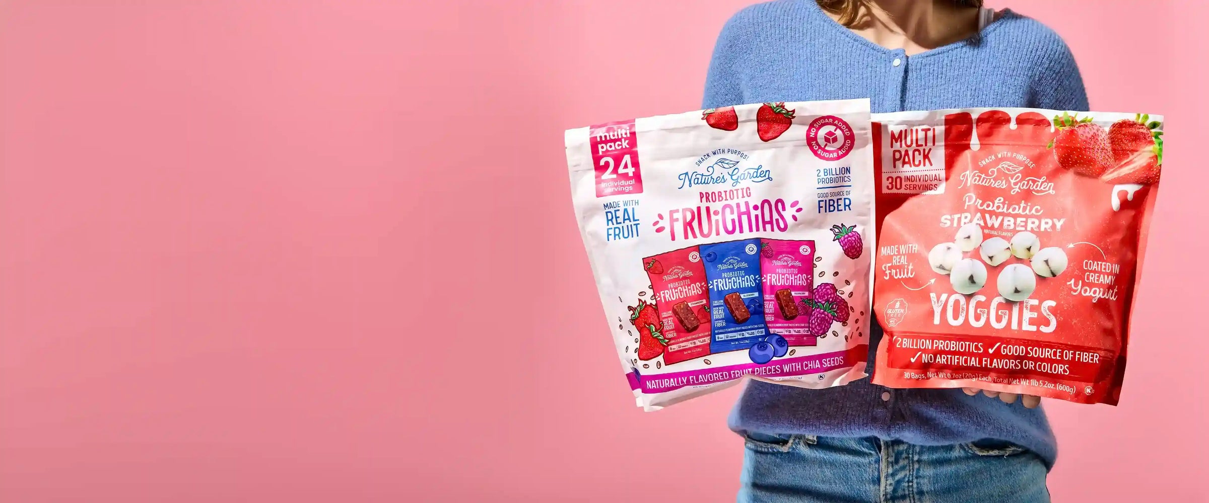 Person holding Nature’s Garden Probiotic FruiChias and Strawberry Yoggies multipacks against a pink background.