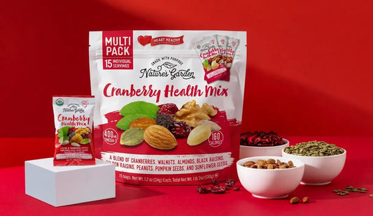 Nature’s Garden Cranberry Health Mix with bowls of walnuts, almonds, pepitas, and dried fruit displayed against a red background.