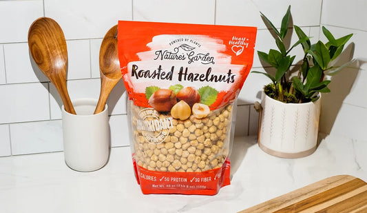 Nature’s Garden Roasted Hazelnuts pouch on a kitchen counter, surrounded by wooden utensils, a plant, and cutting board.