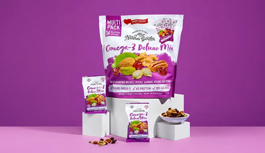 Nature’s Garden Omega-3 Deluxe Mix with almonds, pecans, walnuts, cranberries, pepitas, and pistachios in front of bold purple backdrop.