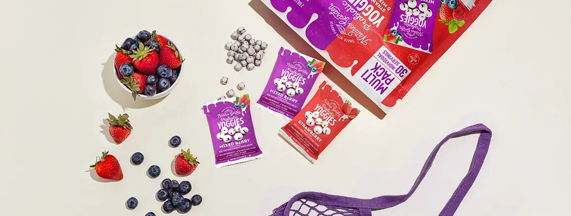 Nature’s Garden Probiotic Yoggies Variety-Pack with strawberry and mixed berry yogurt bites beside fresh fruit and scattered snacks.